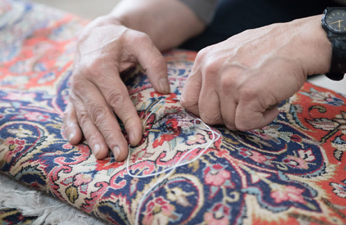 A person is repairing a hole in a rug