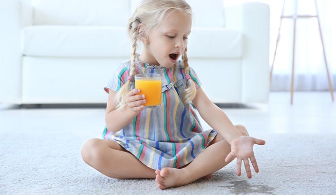 a children sitting on the rug with a glass of orange juice