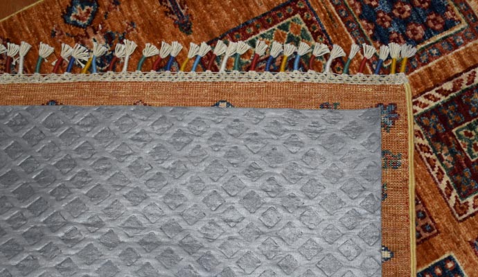 A close-up view of a rug placed on top of rubber rug pad, which is visible underneath.