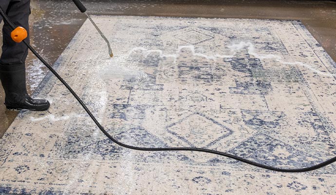 a professional worker uses a high-pressure hose to rinse a large area rug