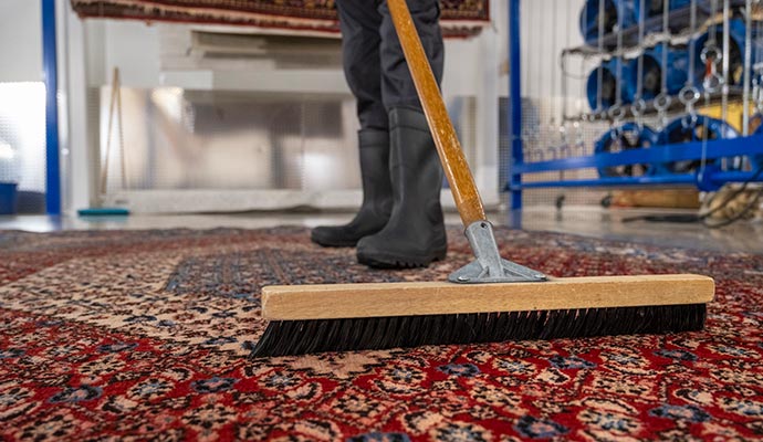 a professional worker cleaning a tibetan rug with a wooden brush